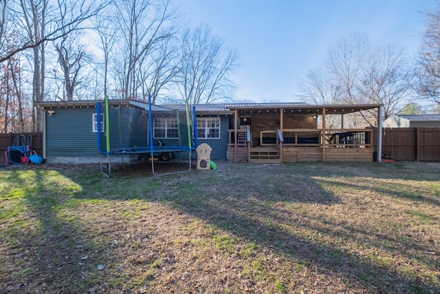 rear view of property featuring a lawn, a deck, and a trampoline