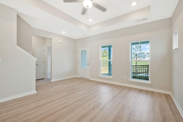 empty room with ceiling fan, light hardwood / wood-style flooring, and a tray ceiling