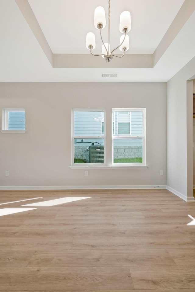 spare room featuring a chandelier, light wood-type flooring, and a tray ceiling