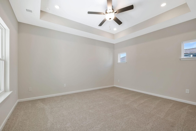 spare room featuring a tray ceiling, ceiling fan, and a healthy amount of sunlight