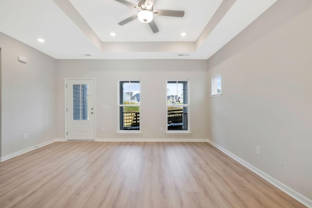 unfurnished room with light wood-type flooring, a raised ceiling, and ceiling fan