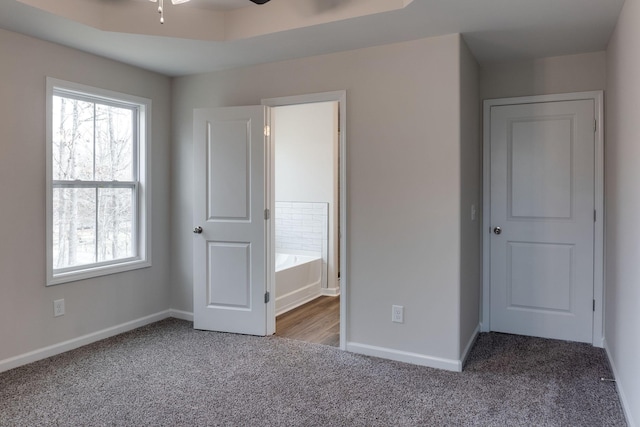 unfurnished bedroom featuring a tray ceiling, ceiling fan, and carpet