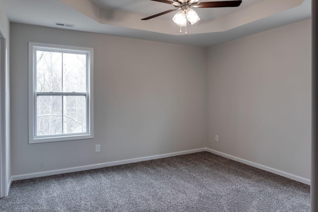 empty room with a tray ceiling, ceiling fan, and carpet flooring