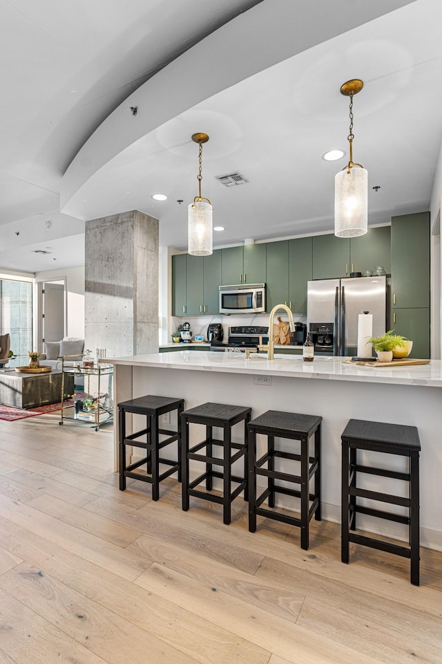 kitchen with a kitchen breakfast bar, stainless steel appliances, light hardwood / wood-style flooring, and green cabinets