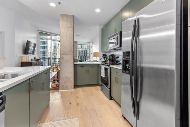 kitchen with appliances with stainless steel finishes, light hardwood / wood-style flooring, expansive windows, and sink