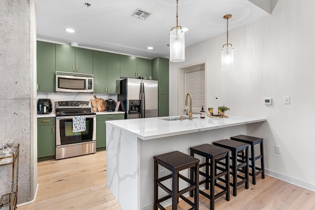 kitchen with kitchen peninsula, a breakfast bar area, appliances with stainless steel finishes, and green cabinetry