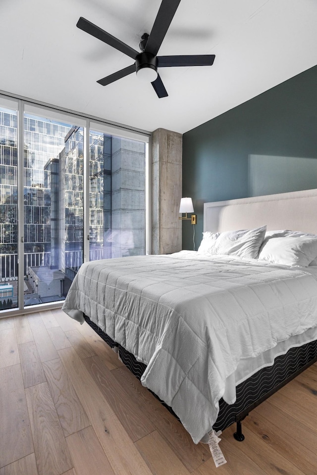 bedroom with access to exterior, ceiling fan, a wall of windows, and hardwood / wood-style flooring