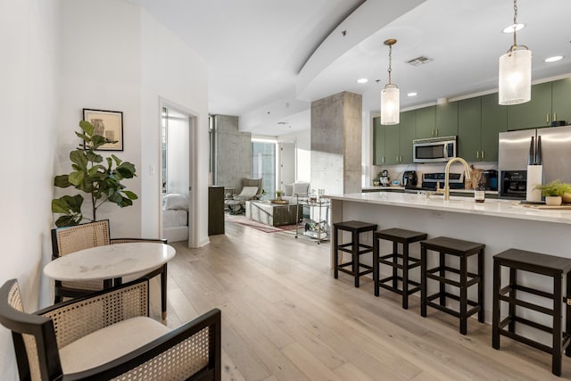 interior space featuring a kitchen breakfast bar, stainless steel appliances, sink, light hardwood / wood-style flooring, and green cabinets