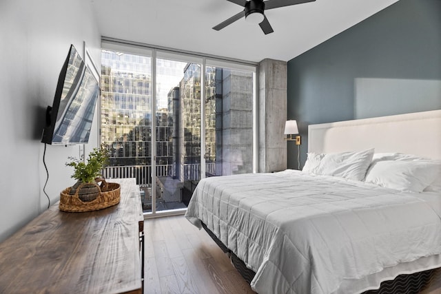 bedroom featuring wood-type flooring, expansive windows, ceiling fan, and access to outside