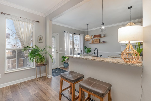 kitchen featuring sink, hanging light fixtures, ornamental molding, light stone countertops, and light wood-type flooring