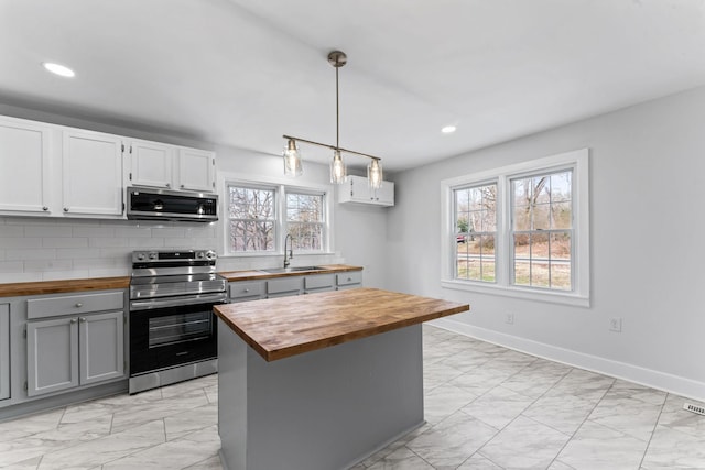 kitchen featuring stainless steel appliances, hanging light fixtures, wood counters, sink, and white cabinetry