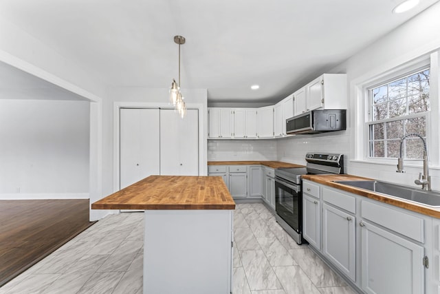 kitchen with decorative light fixtures, stainless steel appliances, wooden counters, backsplash, and sink