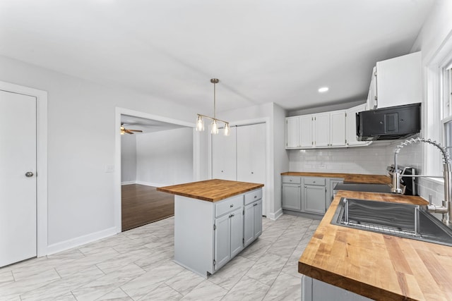 kitchen featuring hanging light fixtures, a center island, wood counters, ceiling fan, and decorative backsplash