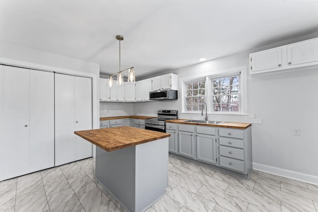 kitchen with butcher block counters, stainless steel appliances, sink, hanging light fixtures, and a kitchen island