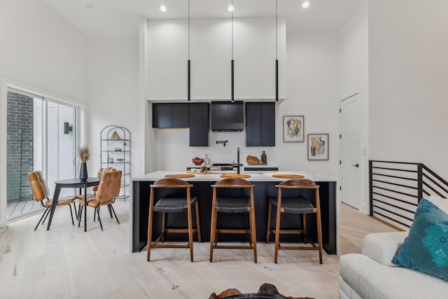 kitchen featuring a high ceiling, backsplash, light hardwood / wood-style floors, and a breakfast bar area