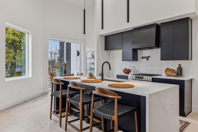 kitchen with stainless steel range, sink, wall chimney exhaust hood, and an island with sink