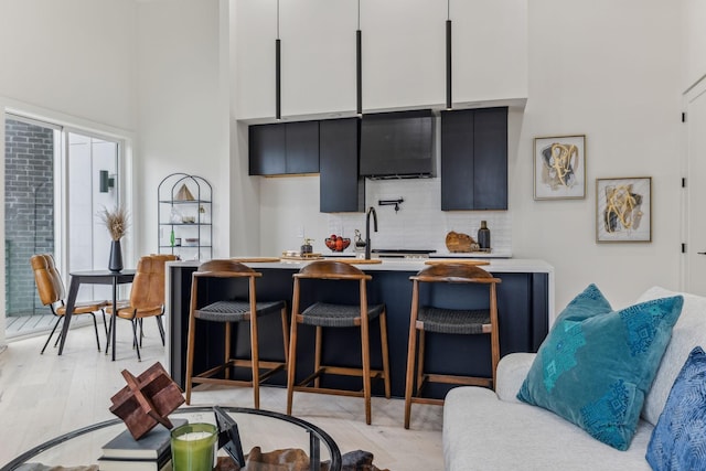 kitchen featuring a kitchen bar, light wood-type flooring, backsplash, sink, and white cabinets