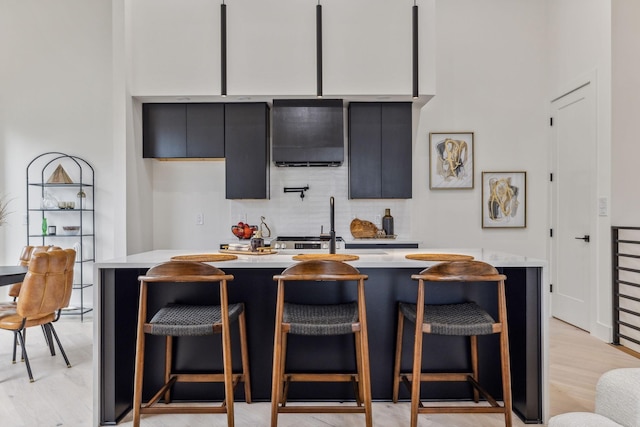 kitchen with a kitchen breakfast bar, backsplash, light hardwood / wood-style flooring, and an island with sink