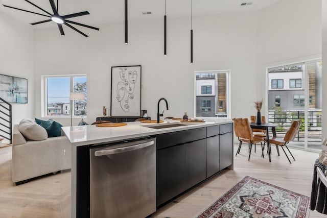 kitchen with a kitchen island with sink, a high ceiling, sink, stainless steel dishwasher, and light hardwood / wood-style floors