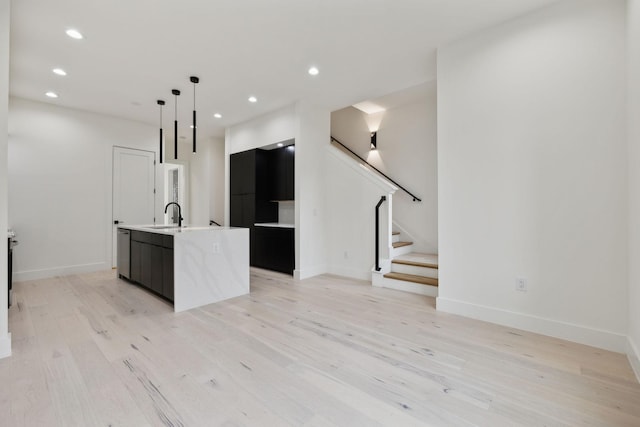 kitchen with sink, decorative light fixtures, light hardwood / wood-style flooring, dishwasher, and an island with sink