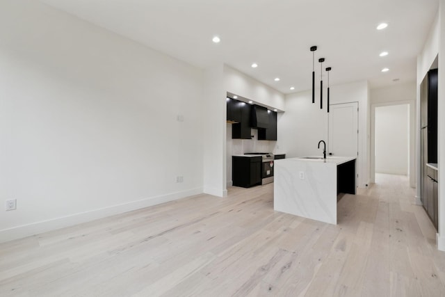 kitchen featuring hanging light fixtures, light wood-type flooring, a kitchen island with sink, and stainless steel range oven