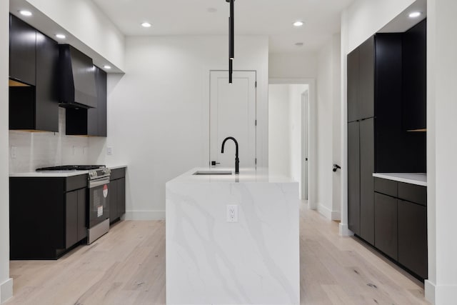 kitchen featuring light wood-type flooring, tasteful backsplash, stainless steel gas range oven, sink, and wall chimney range hood