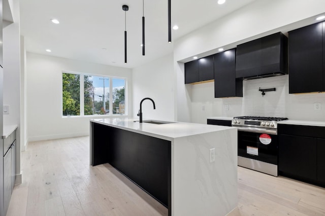 kitchen with sink, stainless steel gas range oven, light hardwood / wood-style flooring, pendant lighting, and a kitchen island with sink