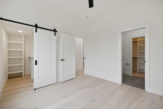 unfurnished bedroom with a barn door, a spacious closet, a closet, and light hardwood / wood-style flooring