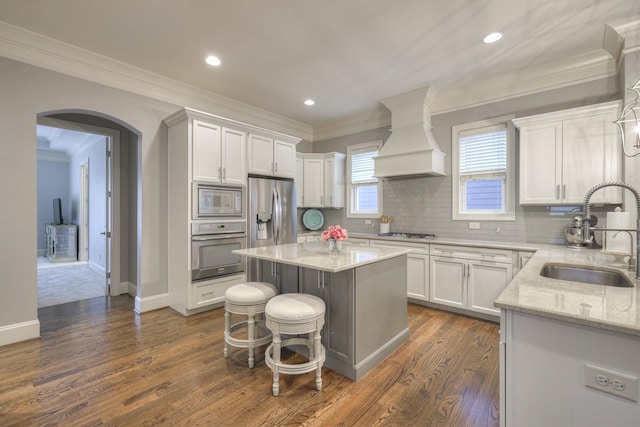 kitchen with white cabinetry, sink, premium range hood, a kitchen island, and appliances with stainless steel finishes