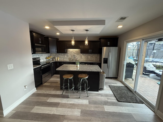 kitchen featuring appliances with stainless steel finishes, backsplash, a breakfast bar, decorative light fixtures, and a center island