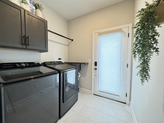 clothes washing area featuring washer and clothes dryer, light tile patterned flooring, and cabinets