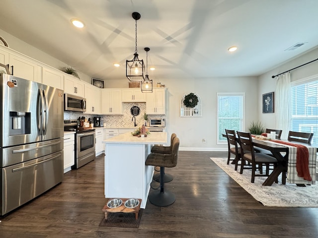 kitchen featuring a center island, white cabinets, a breakfast bar area, decorative light fixtures, and stainless steel appliances