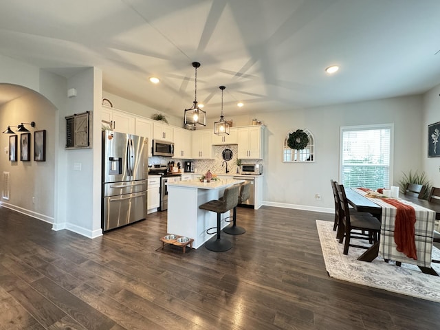 kitchen featuring decorative backsplash, stainless steel appliances, decorative light fixtures, white cabinets, and a kitchen island