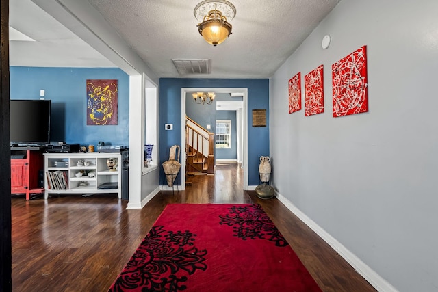 corridor featuring dark hardwood / wood-style floors, a textured ceiling, and an inviting chandelier