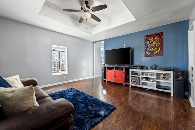 living room with dark hardwood / wood-style flooring, a tray ceiling, and ceiling fan