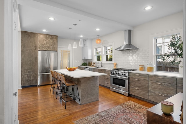 kitchen with a kitchen bar, stainless steel appliances, wall chimney range hood, decorative light fixtures, and a kitchen island