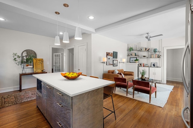 kitchen with hardwood / wood-style floors, ceiling fan, beamed ceiling, dark brown cabinets, and a kitchen island