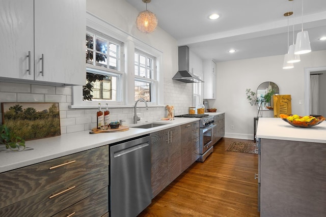 kitchen featuring sink, wall chimney exhaust hood, decorative backsplash, appliances with stainless steel finishes, and decorative light fixtures