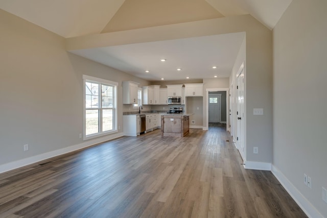 kitchen featuring white cabinetry, a center island, lofted ceiling, appliances with stainless steel finishes, and light wood-type flooring