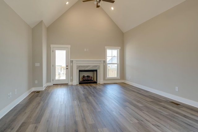 unfurnished living room with ceiling fan, light hardwood / wood-style floors, a premium fireplace, and high vaulted ceiling