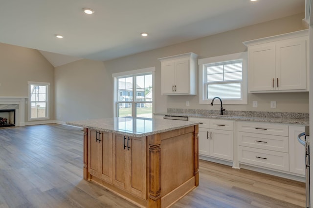 kitchen with a center island, a high end fireplace, white cabinets, light hardwood / wood-style flooring, and light stone counters