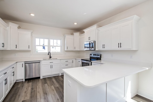 kitchen featuring hardwood / wood-style floors, sink, kitchen peninsula, white cabinetry, and stainless steel appliances