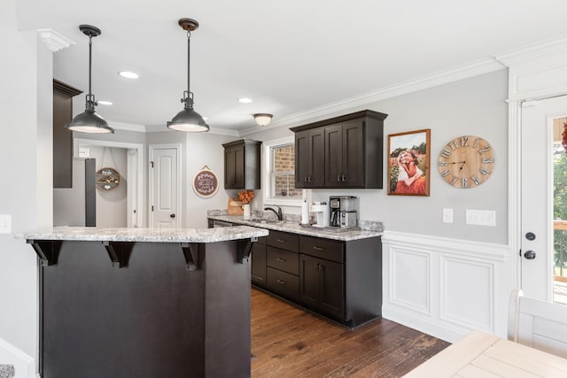 kitchen featuring a kitchen breakfast bar, ornamental molding, dark wood-type flooring, sink, and pendant lighting