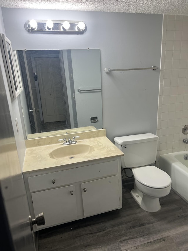 full bathroom with tiled shower / bath combo, a textured ceiling, toilet, vanity, and hardwood / wood-style flooring