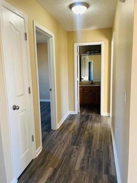 hallway featuring a textured ceiling, dark wood-type flooring, and sink