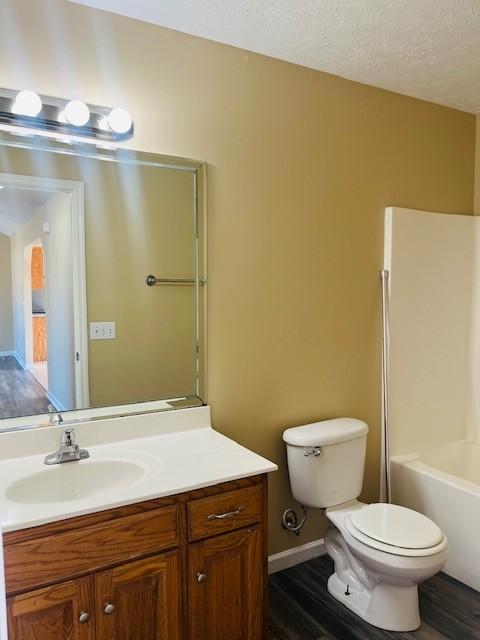 full bathroom with vanity, toilet, a textured ceiling, wood-type flooring, and tub / shower combination