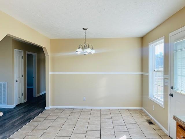 unfurnished dining area featuring light tile patterned floors, a textured ceiling, and an inviting chandelier