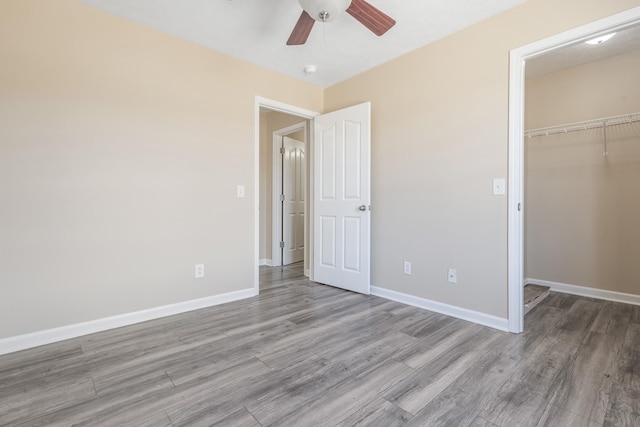 unfurnished bedroom with ceiling fan, a spacious closet, light hardwood / wood-style floors, and a closet