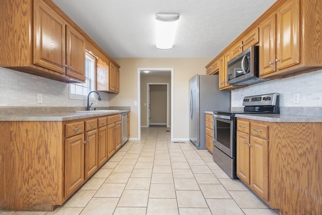 kitchen featuring appliances with stainless steel finishes, sink, decorative backsplash, light tile patterned floors, and a textured ceiling