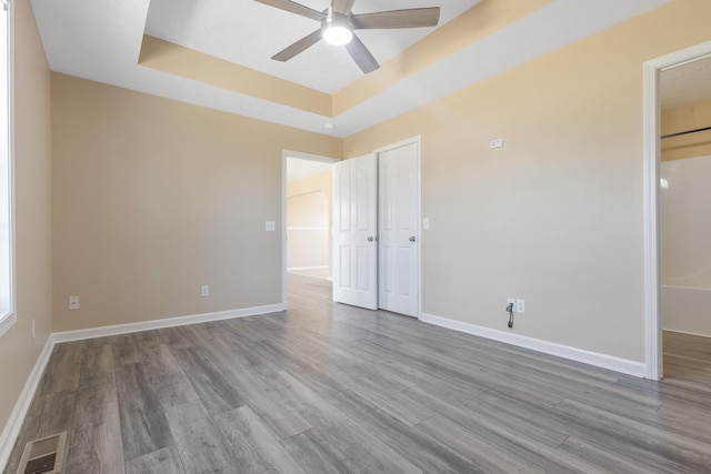 unfurnished bedroom featuring hardwood / wood-style floors, a closet, a raised ceiling, and ceiling fan
